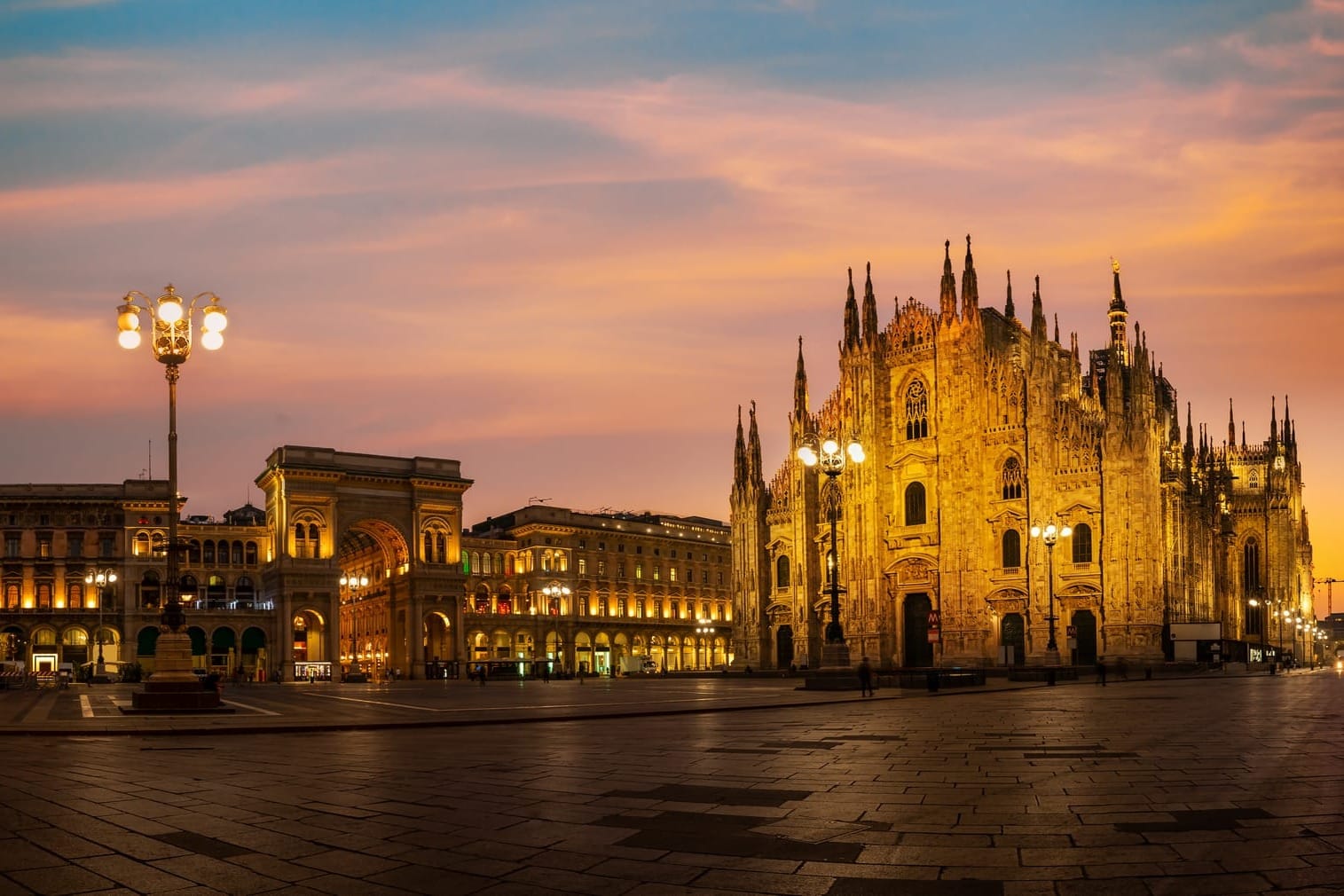 Milan's Piazza Duomo at sunrise, with the iconic Gothic facade of the Duomo cathedral bathed in a soft pink and orange light before the crowds arrive.