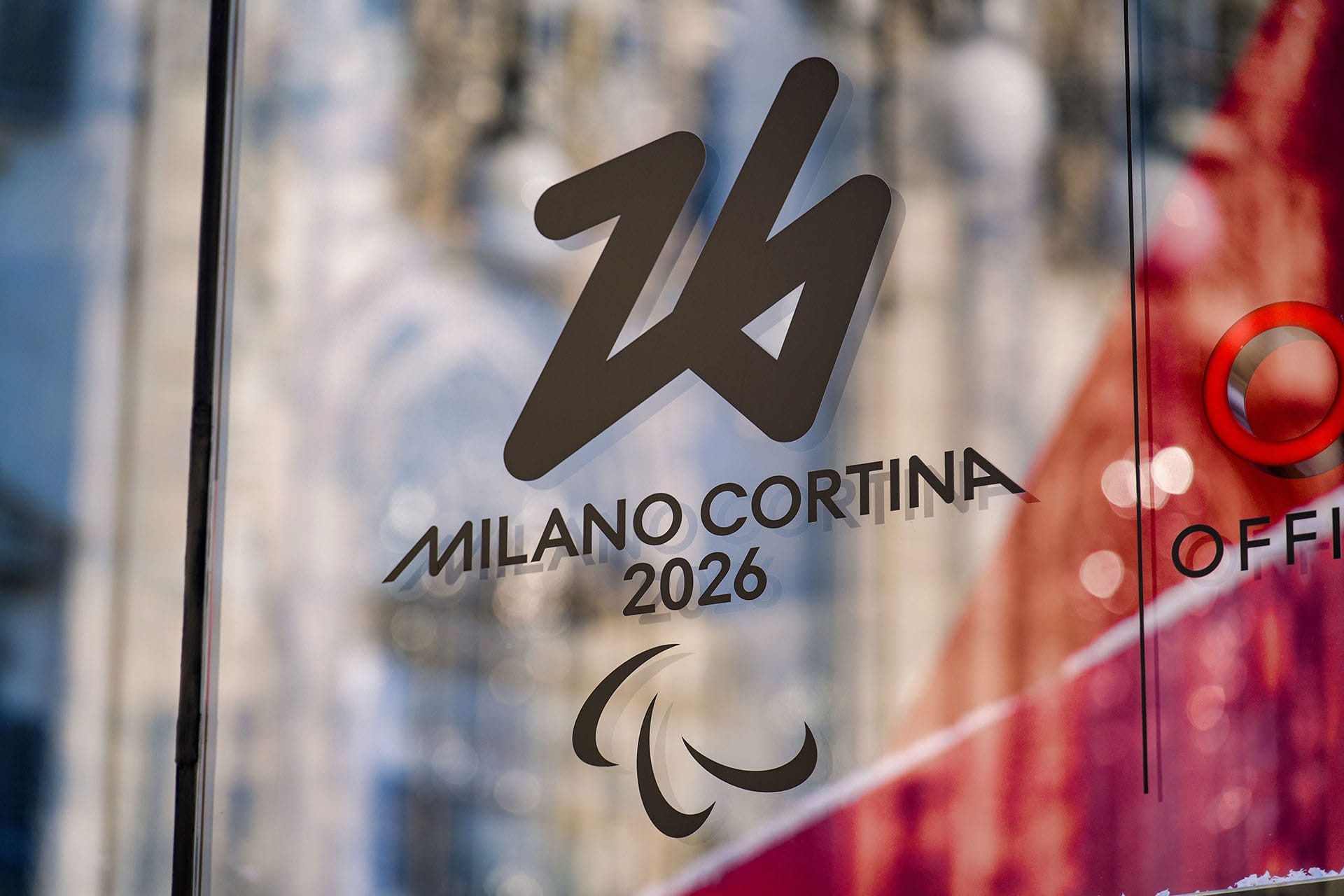 Official Milano Cortina 2026 Winter Olympics logo reflected in the pavement of Milan's Piazza Duomo.