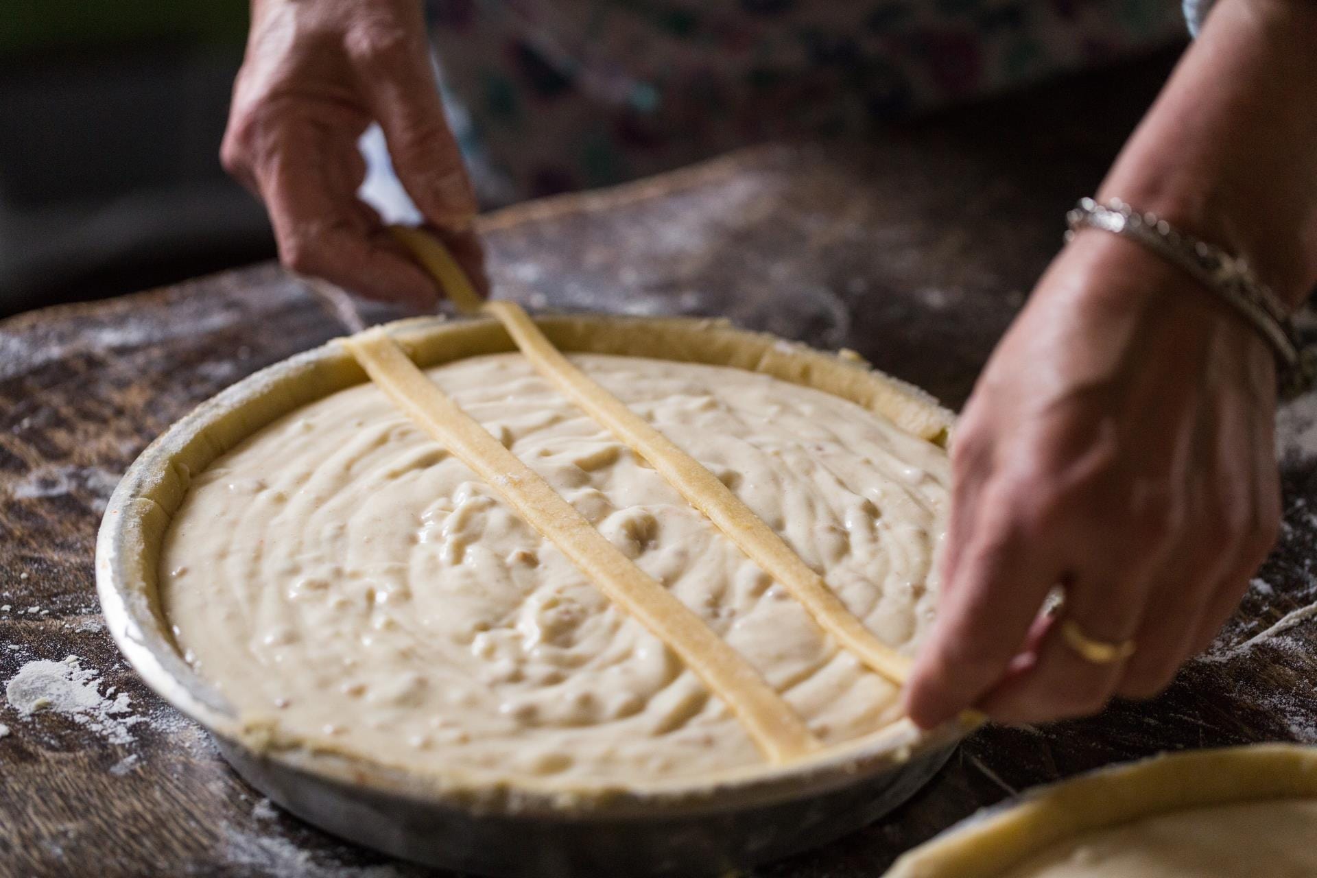 Close-up of hands preparing a traditional Pastiera Napoletana cake with ingredients like cooked wheat, ricotta, and orange blossoms.