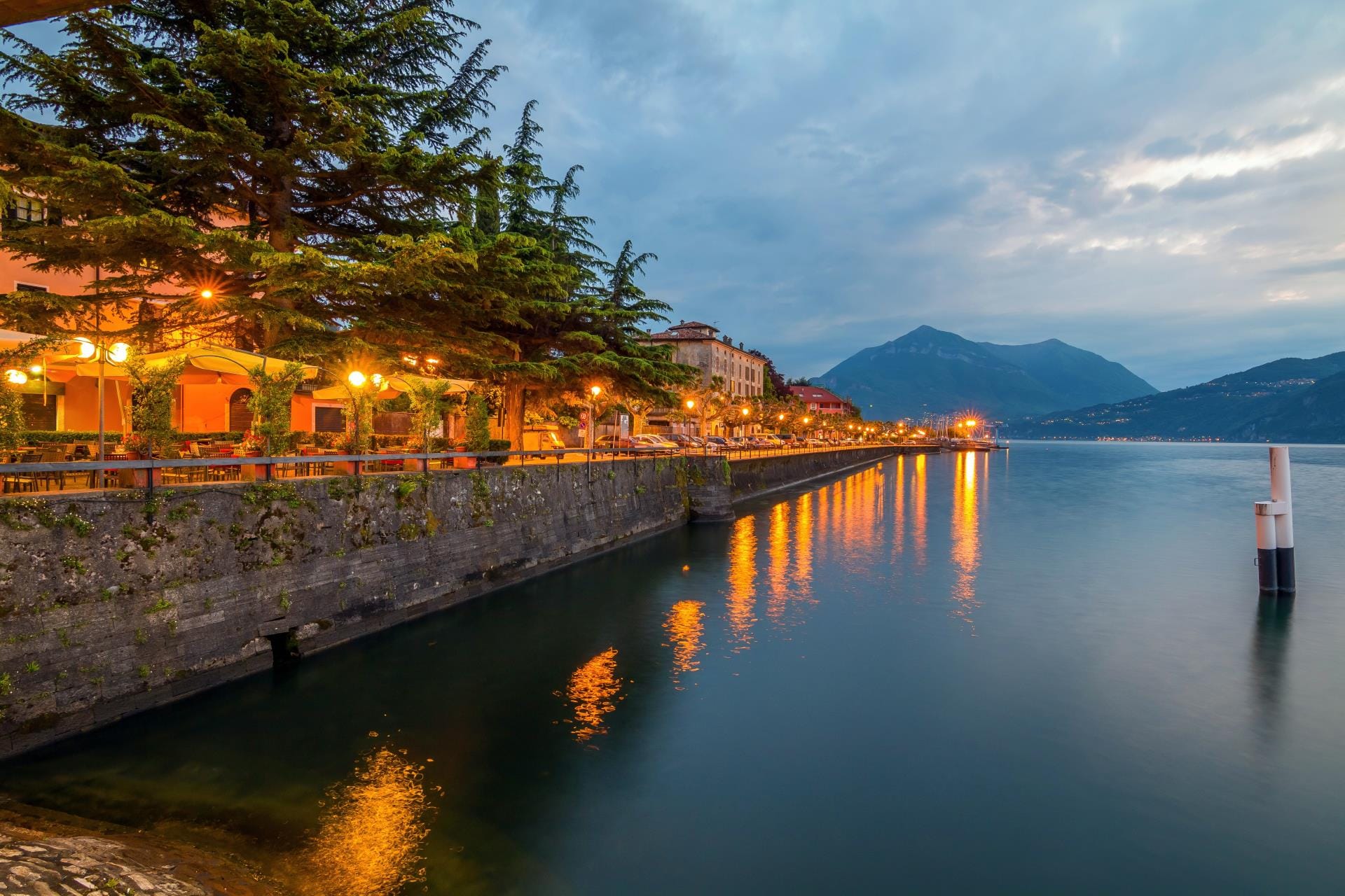 Panoramic view of Bellano village on the shores of Lake Como at sunset with twinkling lights during the winter season.