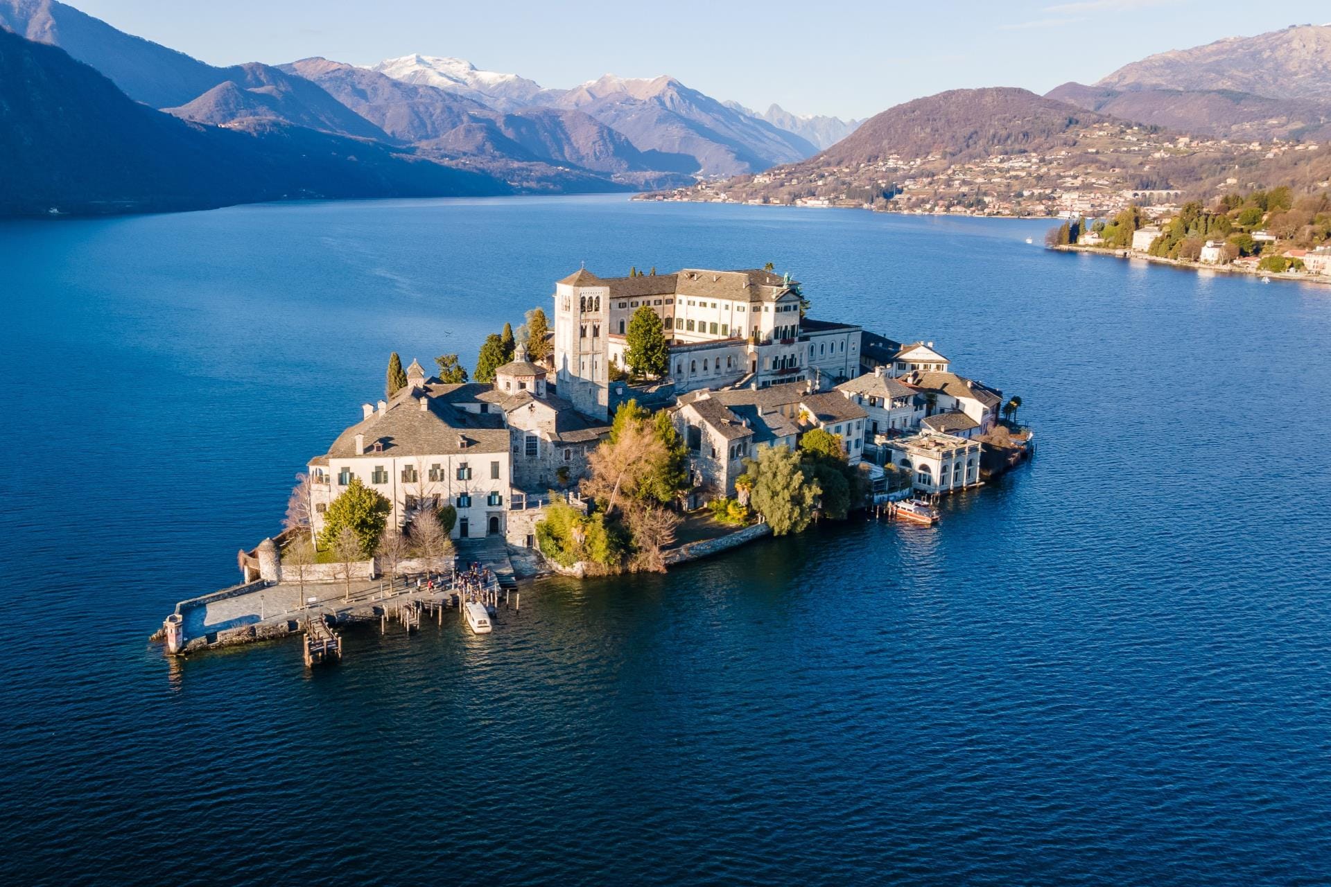 High-angle aerial view of San Giulio island in the center of Lake Orta surrounded by blue water in Northern Italy.