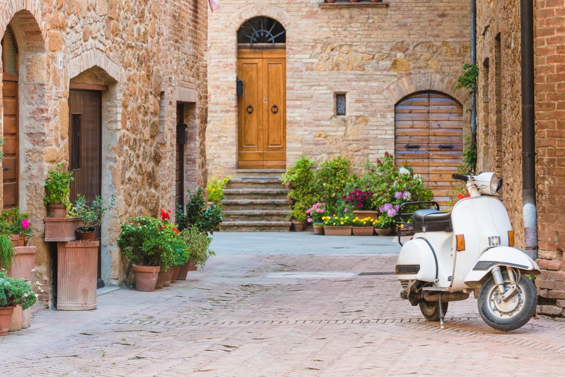 A vintage Vespa scooter parked in a narrow medieval street in a traditional Tuscan hilltop town.
