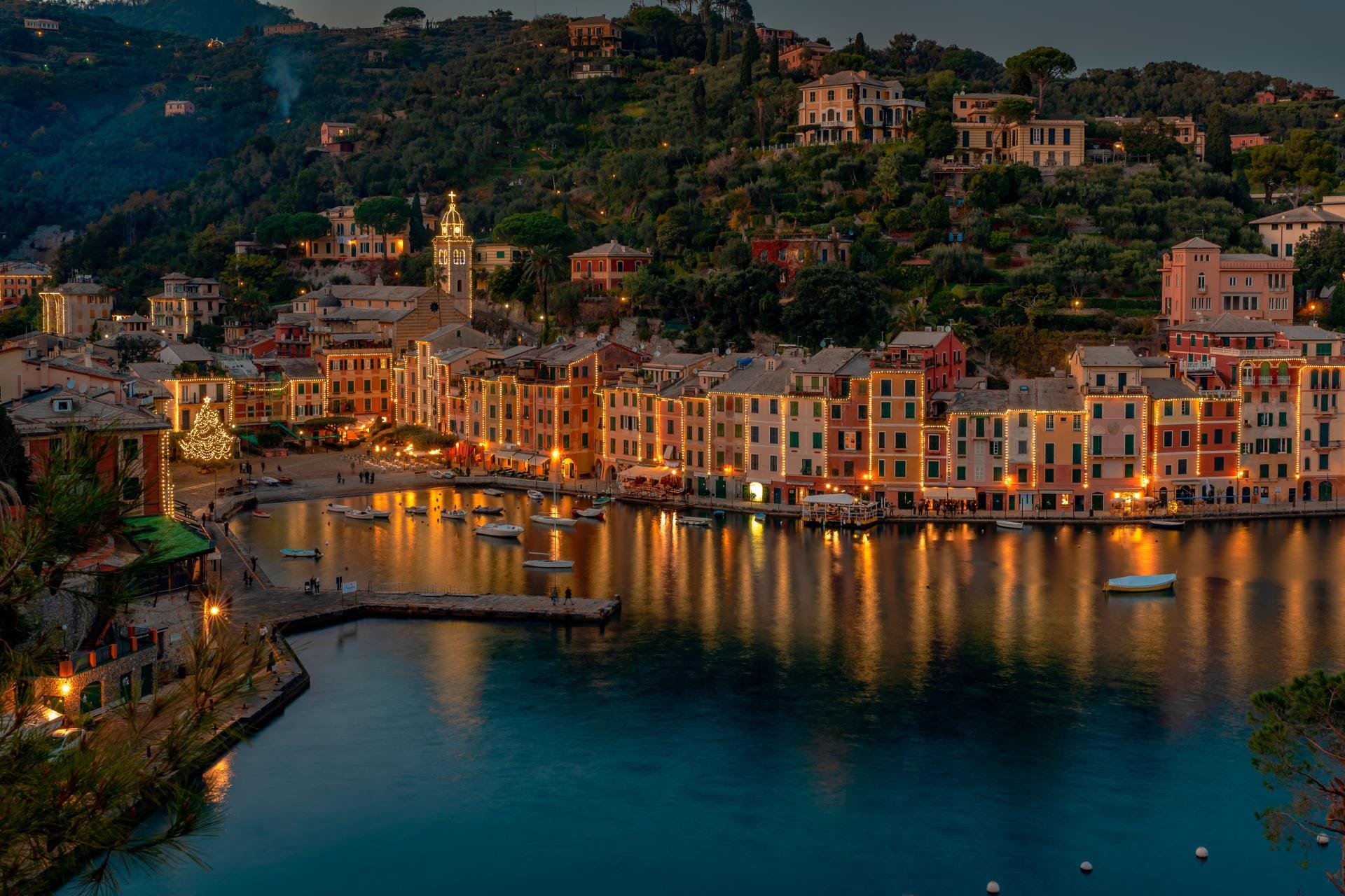 Drone shot of Portofino harbor at twilight with evening lights and a glowing Christmas tree in the main square.