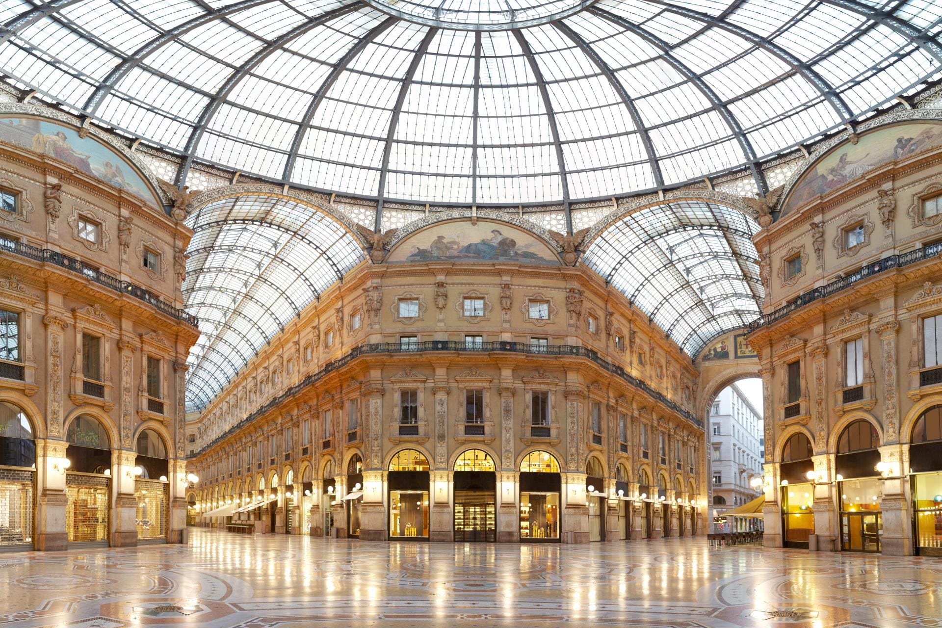 An upward panoramic view of the intricate glass and iron dome and vaulted ceiling of the Galleria Vittorio Emanuele II in Milan.