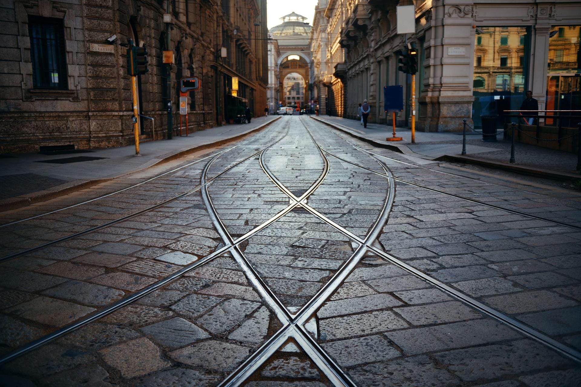 Traditional tram tracks curving through a paved historic street in central Milan, framed by elegant architecture.