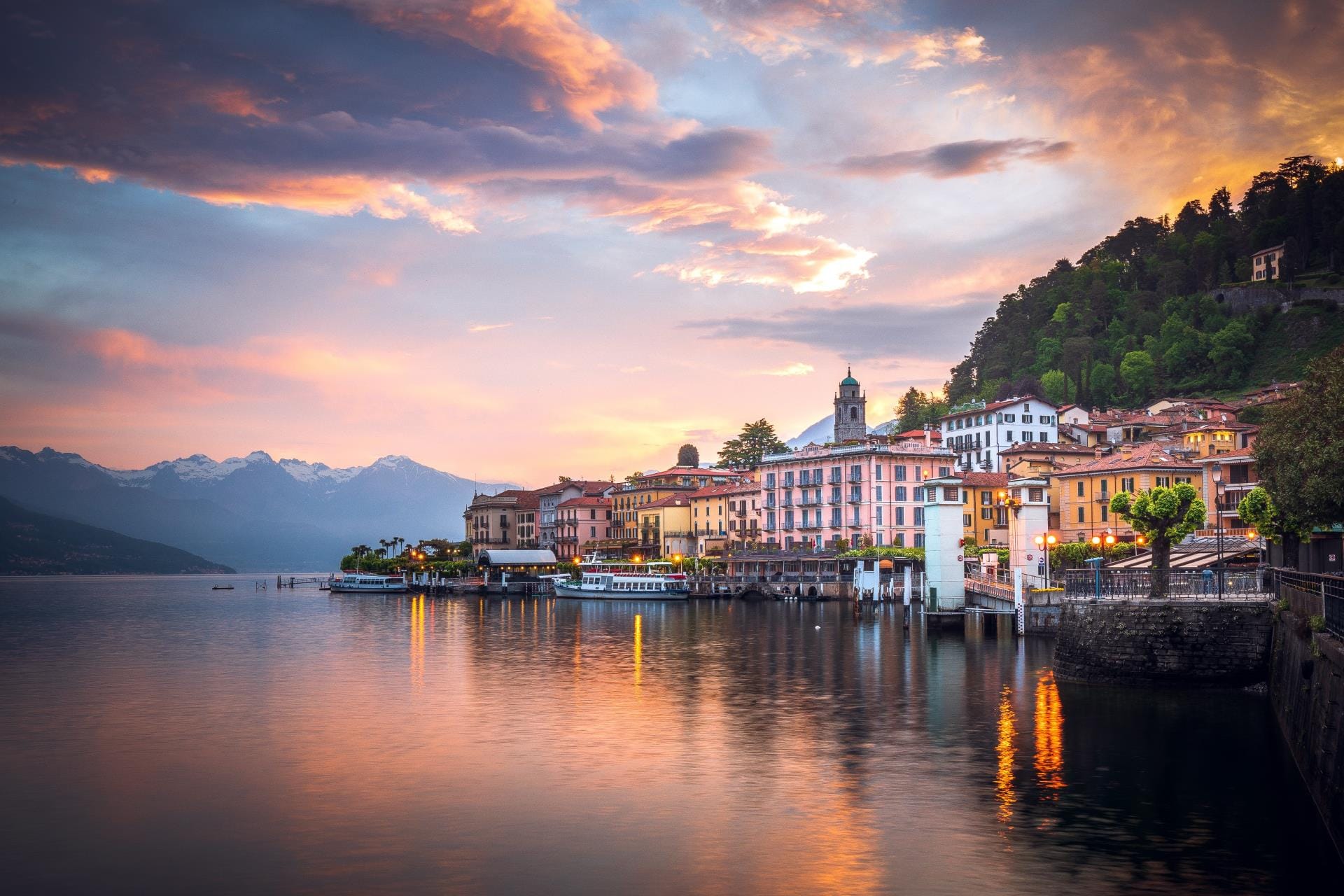Panoramic evening view of the picturesque village of Varenna with warm golden lights illuminating the historic waterfront and the lake shore.
