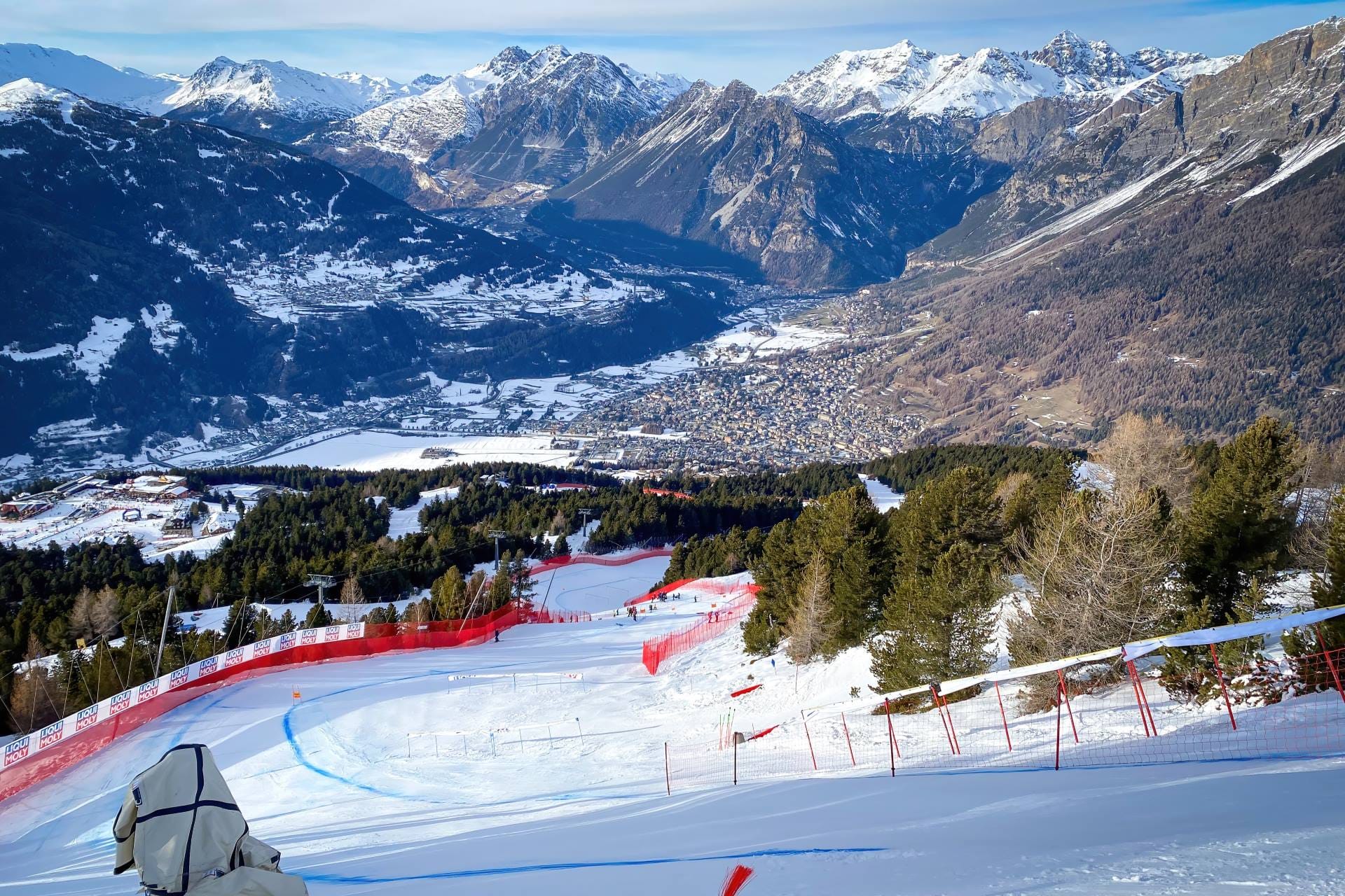 View from the start gate of the Pista Stelvio downhill course in Bormio, looking down the steep slope against a blue sky.