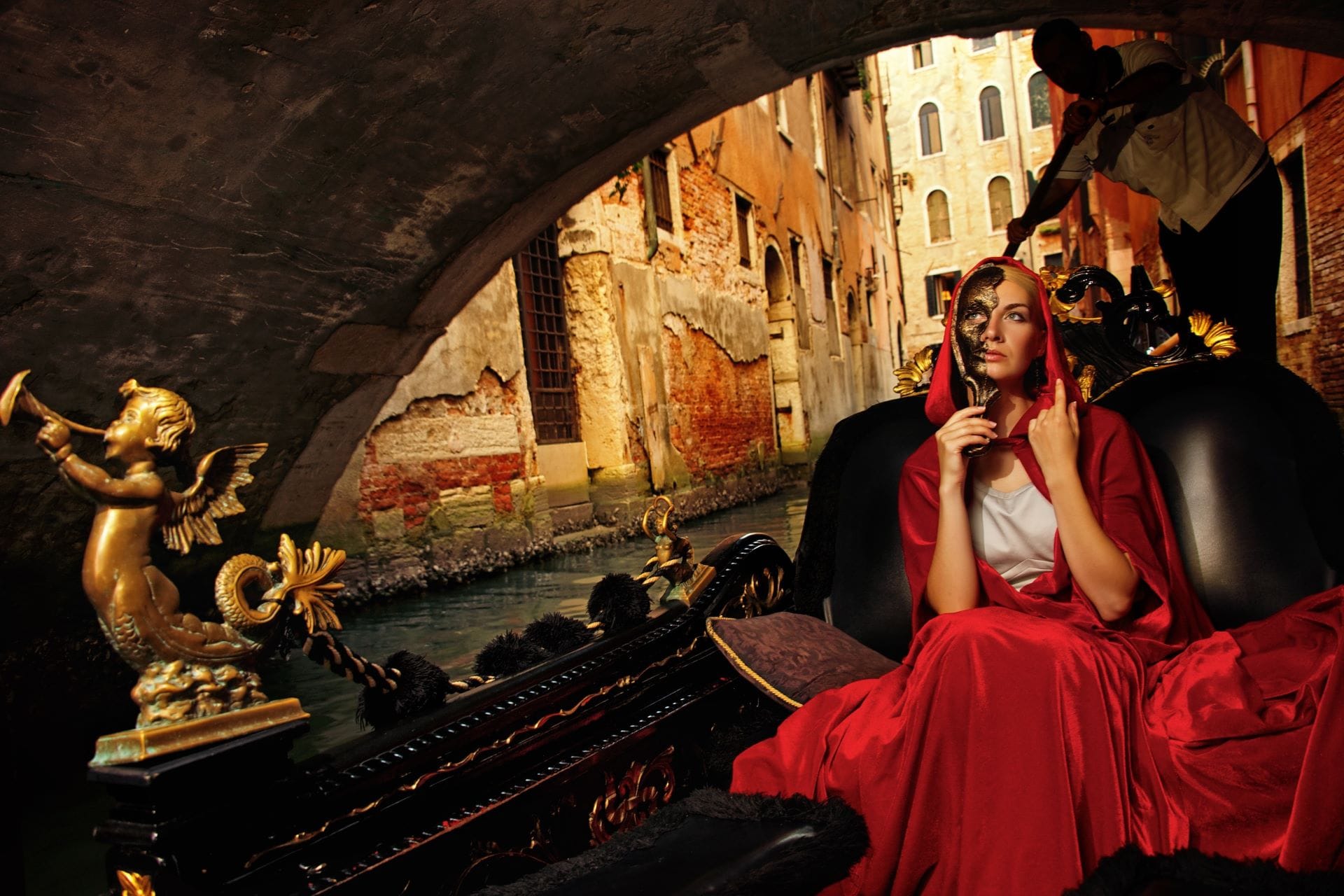 Woman wearing a mysterious red cloak and an elegant Venetian mask riding a traditional gondola on the Grand Canal during Carnival 2026.