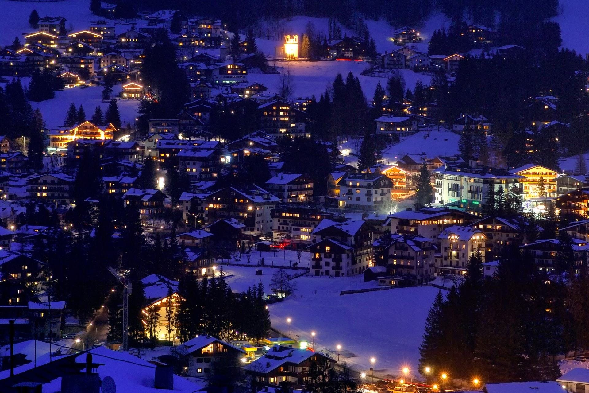 Aerial night photography of the illuminated town of Cortina d'Ampezzo nestled in the snow-covered Ampezzo Valley during winter.