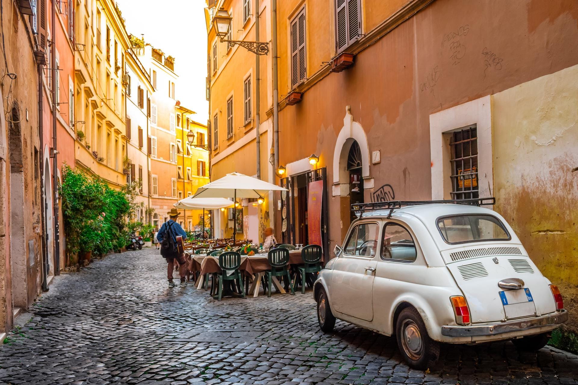 Narrow cobblestone street in the Trastevere neighborhood with ivy-covered buildings and scooters.