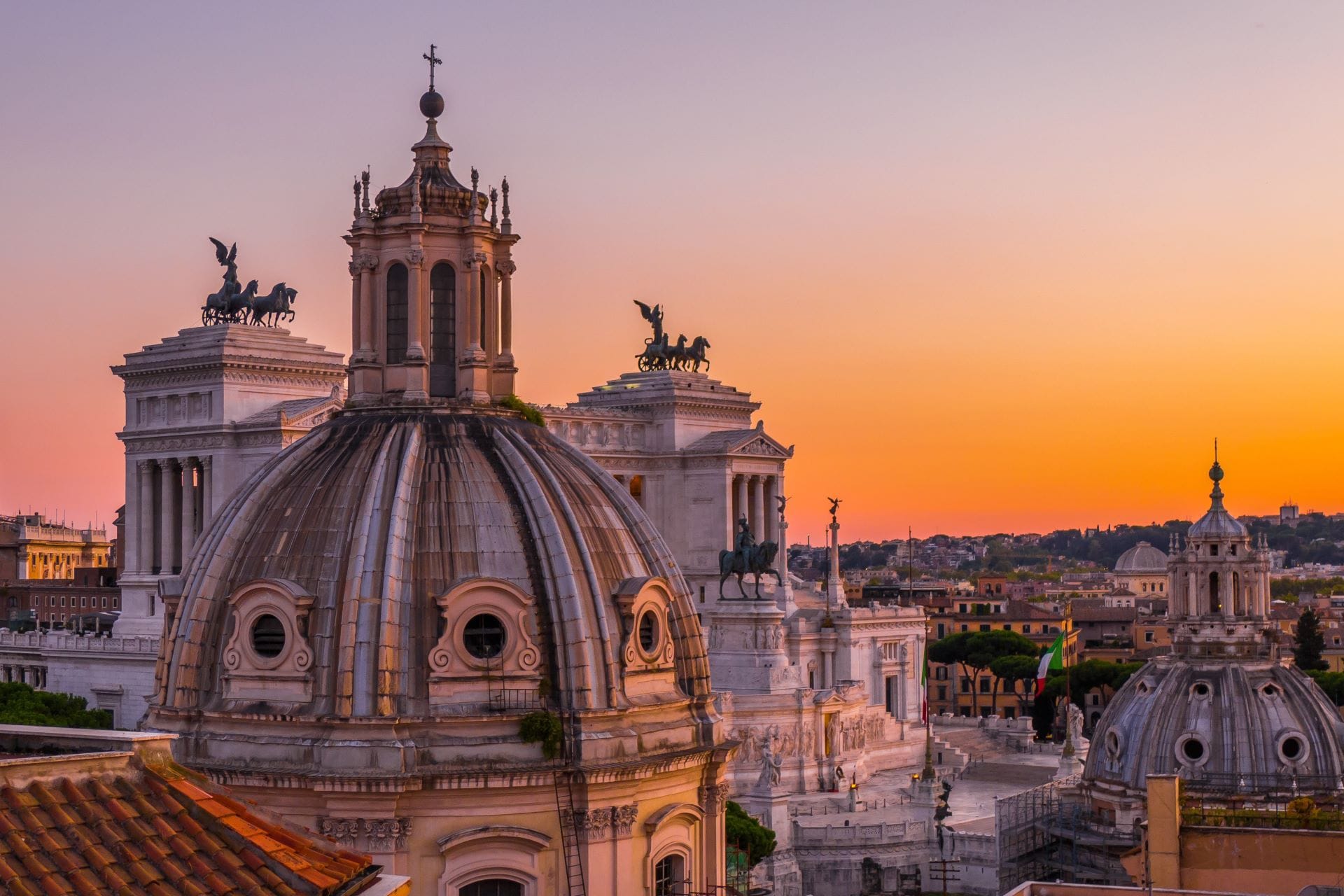 Aerial view of Rome city center rooftops and church domes during a purple and orange sunset.