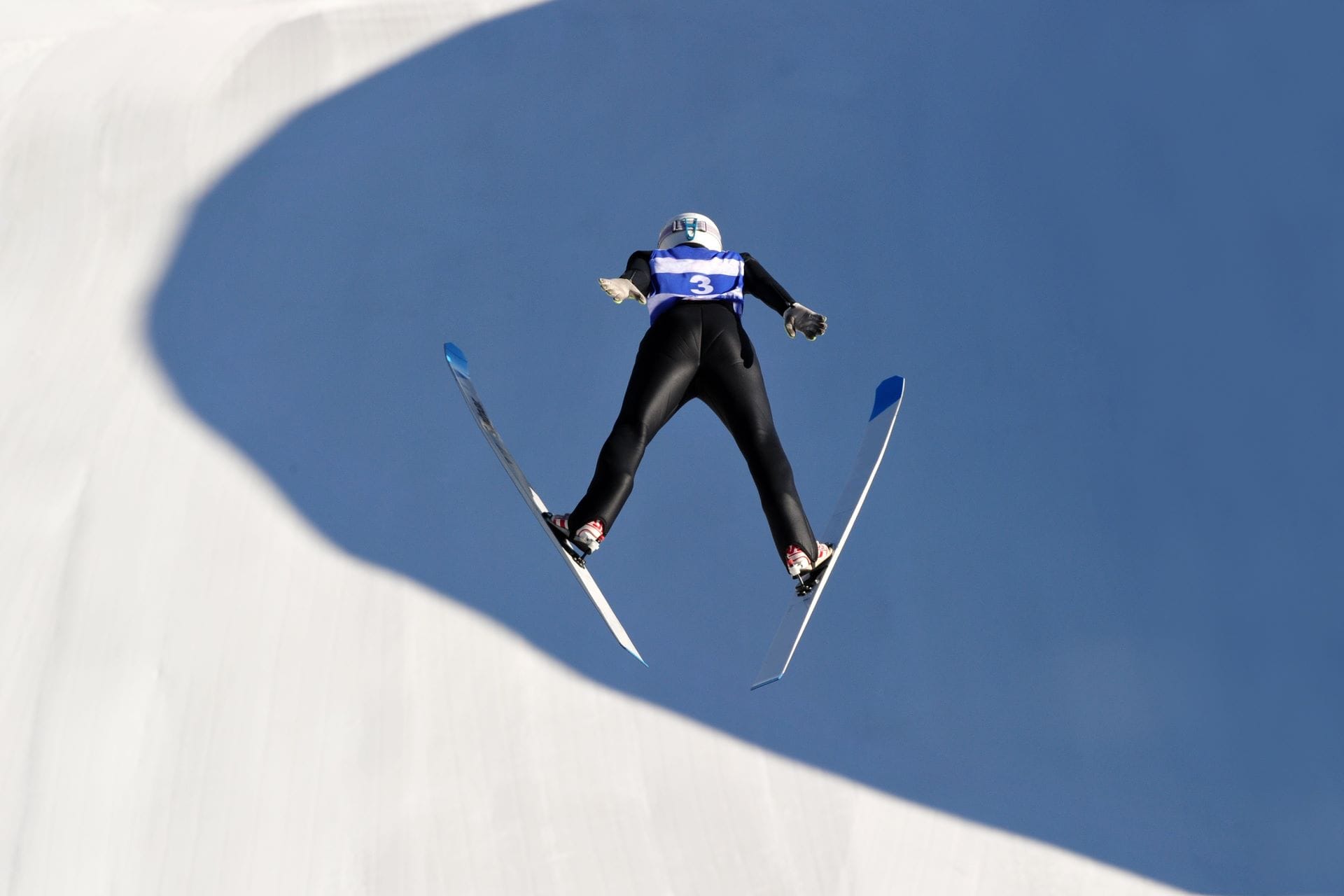 A view from behind the starting gates of a ski jumping hill looking down toward the landing area in Predazzo.
