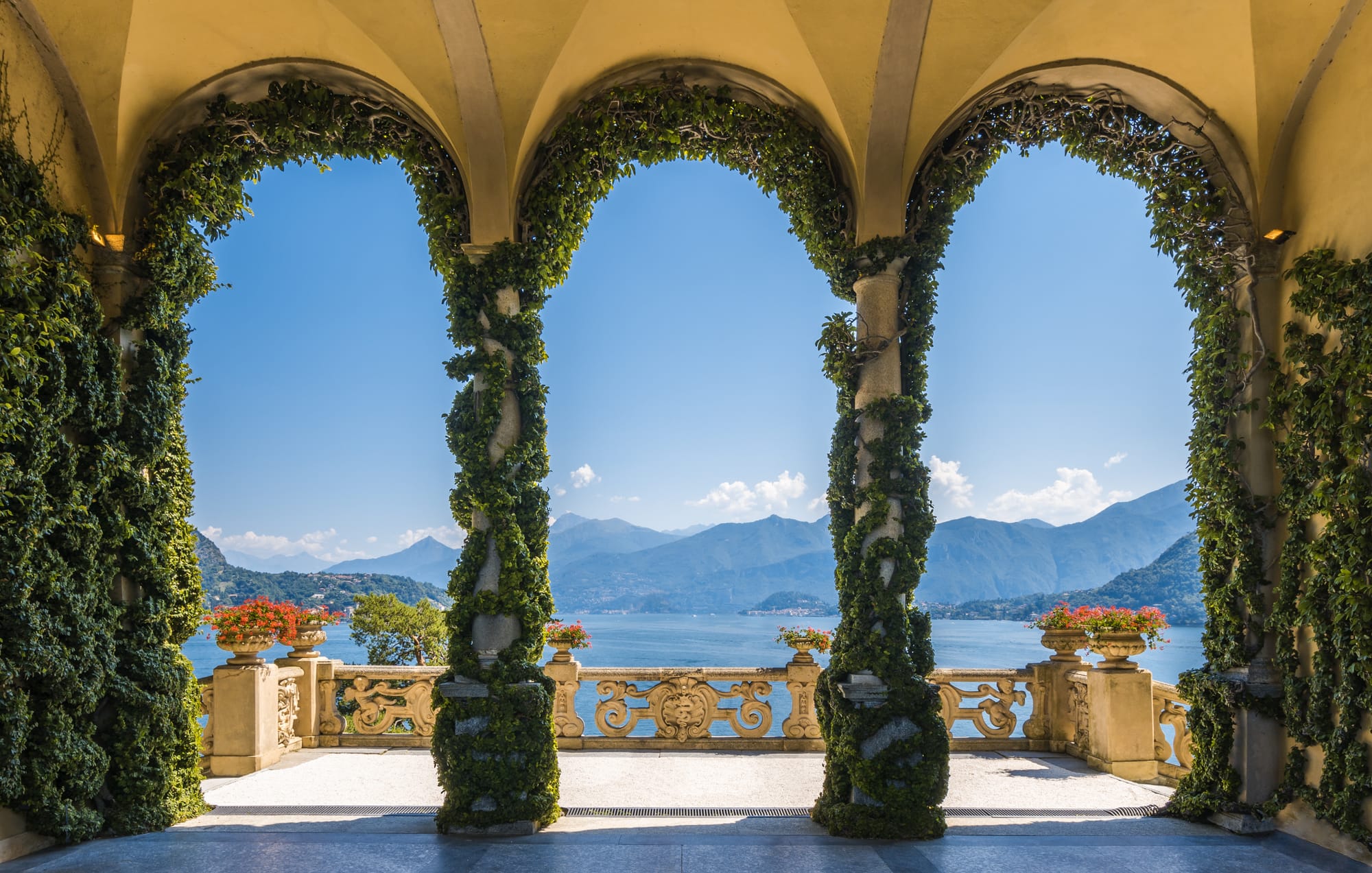 Stunning view of Lake Como, Italy, seen through the stone arches of a classic villa's terrace. A perfect scene from a Lake Como travel guide.